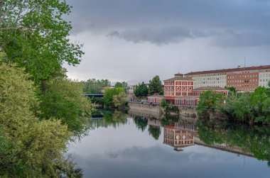 İspanya, La Rioja, Logrono 'daki Ebro Nehri' nin alacakaranlık manzarası nehir kenarındaki binalar ve sıcak akşam ışığı suyu yansıtıyor.