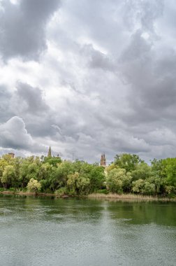 İspanya, La Rioja, Logrono 'daki Ebro Nehri' nin gündüz manzarası, nehir kenarındaki binalar ve gri bulutlu gökyüzü sakin bir şehir manzarası yaratıyor.