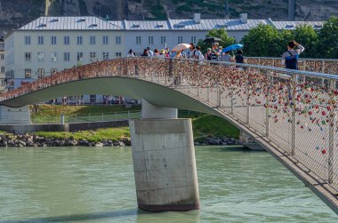 SALZBURG, AUSTRIA - 5 Temmuz 2015: İnsanlar Makartsteg yaya ve bisiklet köprüsünden (2021 'de Marko-Feingold-Steg olarak değiştirildi) Salzach Nehri üzerinden, Salzburg, Avusturya' nın orta kesimindeki aşk kilitleriyle tanınır.