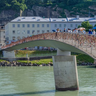 SALZBURG, AUSTRIA - 5 Temmuz 2015: İnsanlar Makartsteg yaya ve bisiklet köprüsünden (2021 'de Marko-Feingold-Steg olarak değiştirildi) Salzach Nehri üzerinden, Salzburg, Avusturya' nın orta kesimindeki aşk kilitleriyle tanınır.