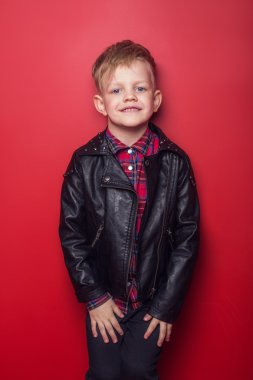 Küçük çocuk bir deri ceket moda. Stüdyo portre kırmızı bir arka plan üzerinde