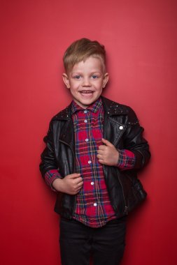Küçük çocuk bir deri ceket moda. Stüdyo portre kırmızı bir arka plan üzerinde