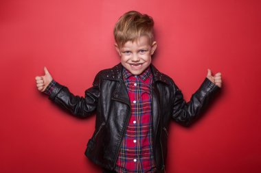 Küçük çocuk bir deri ceket moda. Stüdyo portre kırmızı bir arka plan üzerinde