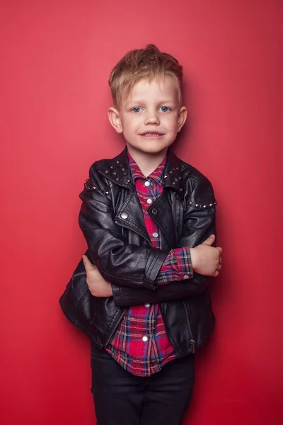 Bambino alla moda in giacca di pelle. Studio ritratto su sfondo rosso — Foto Stock