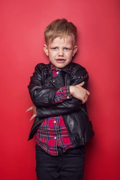 Модный ребенок в кожаной куртке. Студийный портрет на красном фоне — стоковое фото
