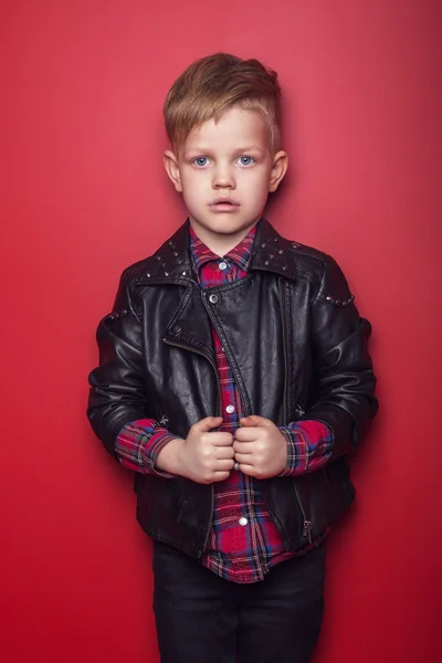 Fashion little boy wearing a leather jacket. Studio portrait over red background — Stock Photo, Image
