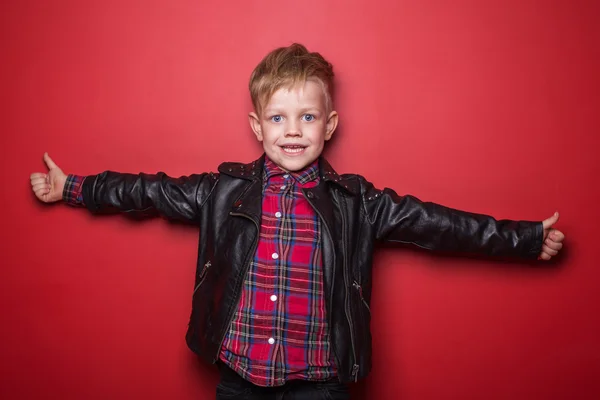 Fashion little boy wearing a leather jacket. Studio portrait over red background — Stock Photo, Image