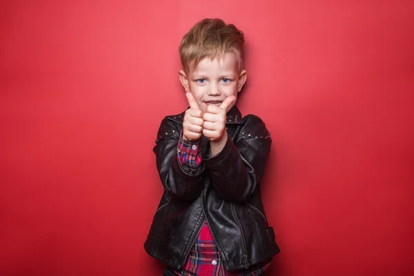 Модный маленький мальчик в кожаной куртке. Студийный портрет на красном фоне — стоковое фото