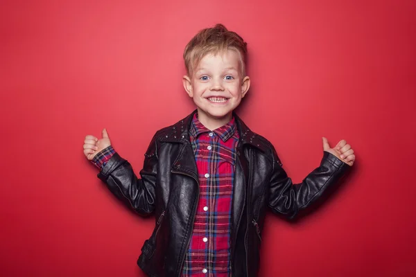 Mode kleiner Junge trägt eine Lederjacke. Studioporträt über rotem Hintergrund — Stockfoto