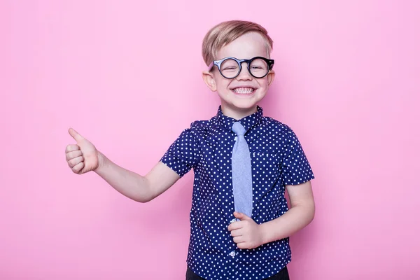 Retrato de un niño sonriente con unas gafas y corbata graciosas. De acuerdo, la escuela. Preescolar. Moda. Estudio retrato sobre fondo rosa — Foto de Stock