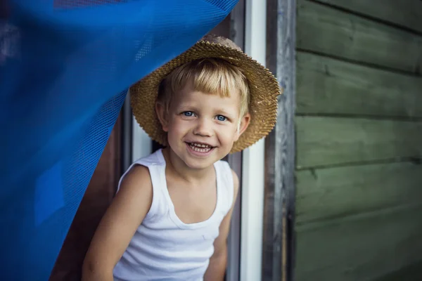 Ragazzo allegro con cappello di paglia appoggiato fuori da una finestra — Foto Stock