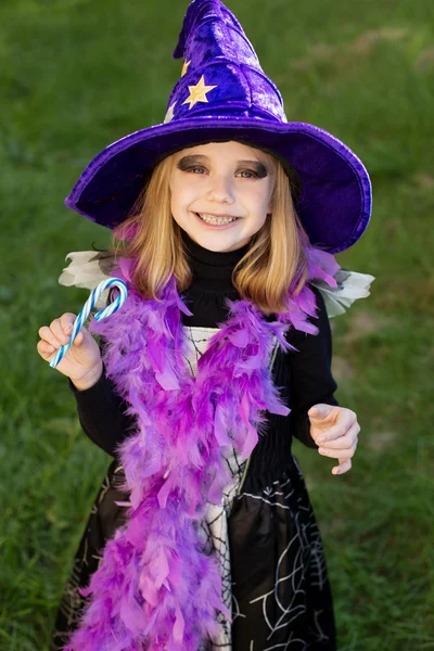 Malá krásná dívka s halloween čarodějnice kostým usmívá a mají barevné bonbóny — Stock fotografie