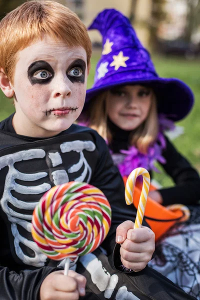 Halloween. Esqueleto y bruja sosteniendo caramelos coloridos —  Fotos de Stock