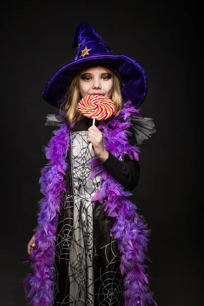 Kleines schönes Mädchen mit Halloween-Hexenkostüm essen farbige Süßigkeiten — Stockfoto