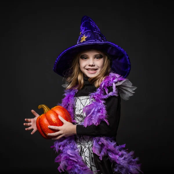 Sevimli küçük Halloween cadı bir turuncu kabak holding — Stok fotoğraf