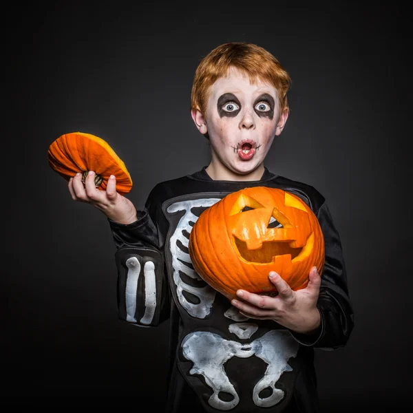 Verrast rood haar kind in Halloween kostuum houden een oranje pompoen. Skelet — Stockfoto