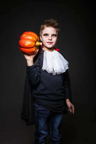 Lindo niño vestido como un vampiro para la fiesta de Halloween y la celebración de una calabaza naranja —  Fotos de Stock