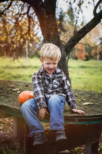 Beautiful casual blond child sitting outdoor on table and laughing. Autumn — Stock Photo, Image