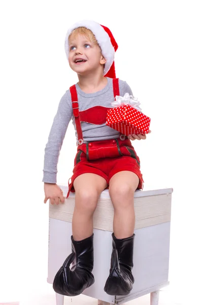 Little child in red costume of dwarf holding gift box with ribbon and looking up. Christmas — Stock Photo, Image