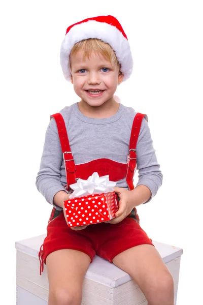 Niño rubio con traje rojo de enano sosteniendo caja de regalo con cinta. Navidad — Foto de Stock