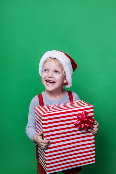 Riendo niño divertido en Santa sombrero rojo sosteniendo regalo de Navidad en la mano. Concepto de Navidad — Foto de Stock