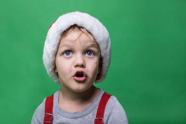 Překvapený dítě s červenou čepici Santa Claus vzhlédl. Velké modré oči. Vánoční koncepce — Stock fotografie