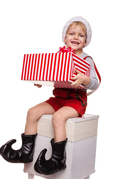Sarışın çocuk büyük hediye kutusu kurdele ile tutarak cüce Kırmızı kostümlü. Noel kavramı — Stok fotoğraf