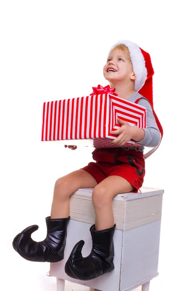 Niño bonito con traje de ayudante de Santa Claus sosteniendo gran caja de regalo a rayas y mirando hacia arriba — Foto de Stock