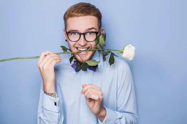 Atractivo joven sonriendo con una rosa blanca en la boca. Fecha, cumpleaños, San Valentín — Foto de Stock