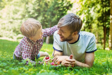 Summer photo happy father and son together lying on green grass. Life moment family resting on the nature