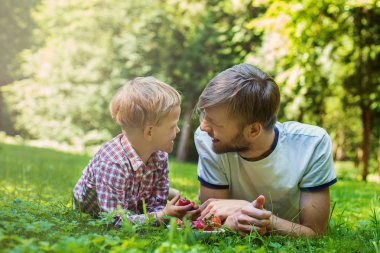 Summer photo happy father and son together lying on green grass. Life moment family resting on the nature