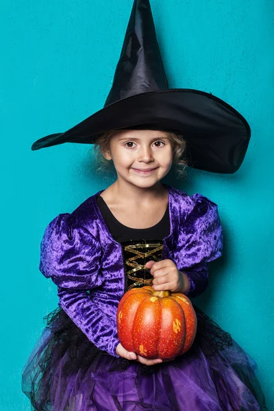 Portrait of little girl in black hat and witch clothing with pumpkin. Halloween. Fairy. Tale. Studio portrait on blue background — Stock Photo, Image