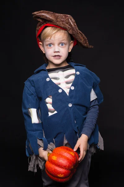 Маленький мальчик в костюме пирата на Хэллоуин позирует с тыквой на черном фоне. Студийный портрет — стоковое фото