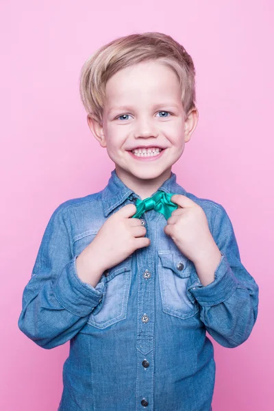 Young beautiful boy with blue shirt and butterfly tie. Studio portrait over pink background — Stock Photo, Image