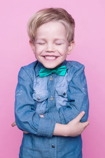 Jovem menino bonito com camisa azul e gravata borboleta. Retrato de estúdio sobre fundo rosa — Fotografia de Stock