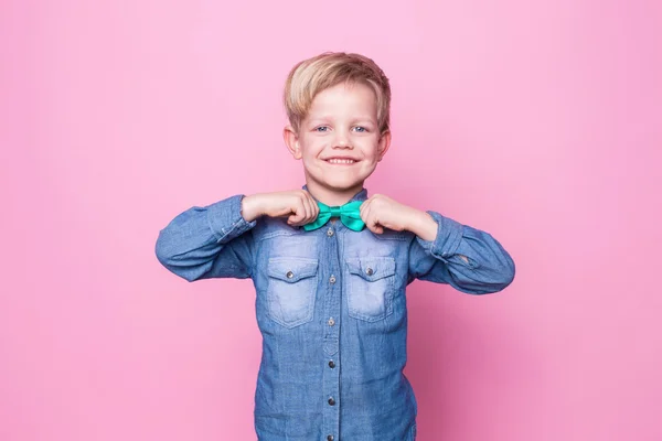 Ung stilig unge som ler med blå skjorta och fjärilsslips. Studio porträtt över rosa bakgrund — Stockfoto