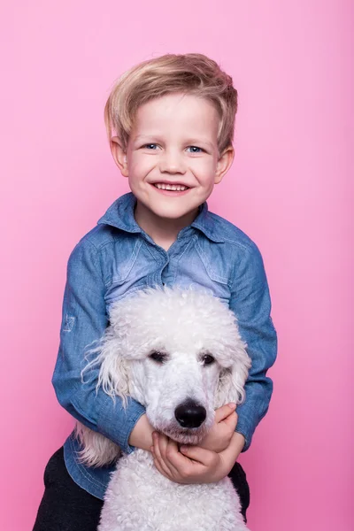 Vackra pojke med Royal pudel. Studio porträtt över rosa bakgrund. Koncept: vänskap mellan pojke och hans hund — Stockfoto