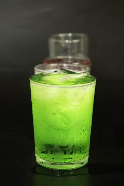 Kırmızı ve yeşil süt ve bir siyah arka plan üzerine bir bardak buz.