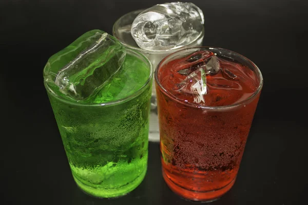 Água vermelha e verde e gelo em um copo em um fundo preto . — Fotografia de Stock