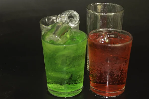 Κόκκινο και πράσινο νερό και τον πάγο σε ένα ποτήρι πάνω σε μαύρο φόντο. — Φωτογραφία Αρχείου