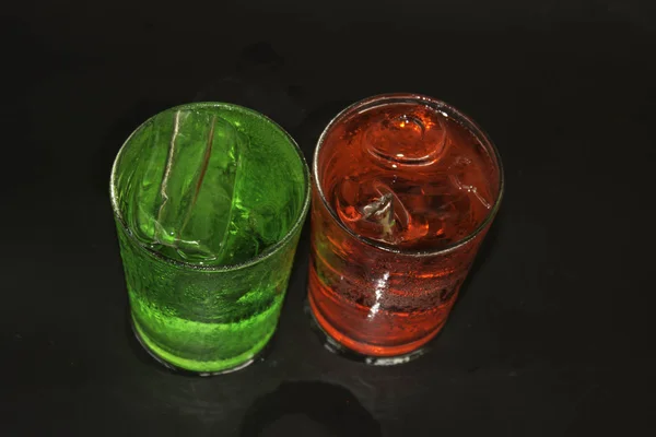 Agua roja y verde y hielo en un vaso sobre un fondo negro . — Foto de Stock