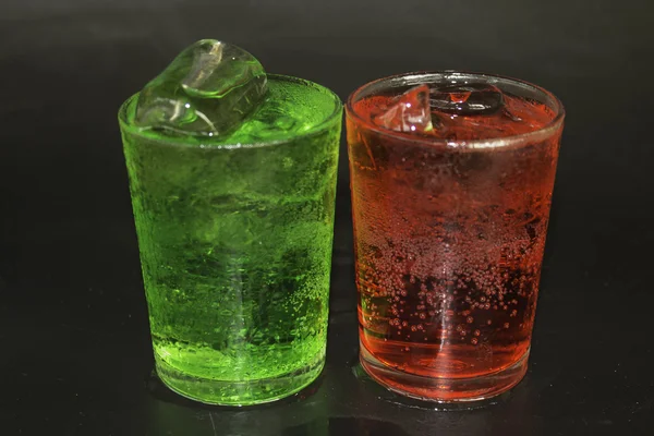 Água vermelha e verde e gelo em um copo em um fundo preto . — Fotografia de Stock