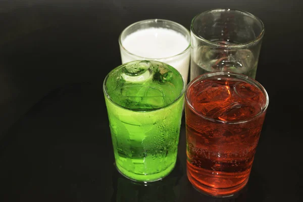 Leite vermelho e verde e gelo em um copo em um fundo preto . — Fotografia de Stock