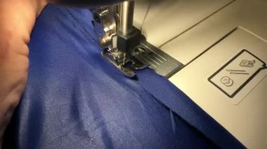 İşçi dikiş makinesine bez dikiyor. Kumaştaki ipliği ayırır.