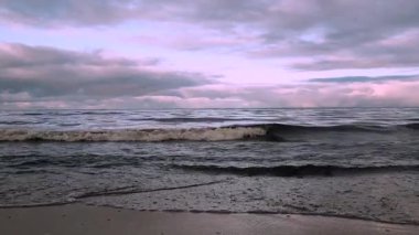 Fırtınalı denizin gün batımında ufka olan görüntüsü. Sörf köpüğü kıyıları şiddetli dalgalarla yıkar..