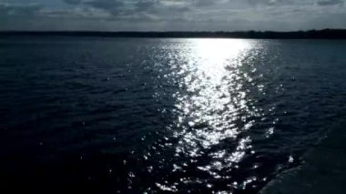 Karanlık suyun üzerinde gün batımı. Güneşin altında parlayan bir deniz manzarası..