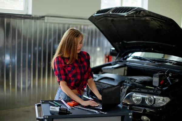 Kobiece mechanik w kraciastej koszuli, w pracy. Auto service station. — Zdjęcie stockowe