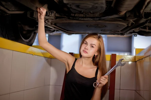 Młoda seksowna brunetka mechanik w kraciastej koszuli w samochodzie Naprawa pit. — Zdjęcie stockowe