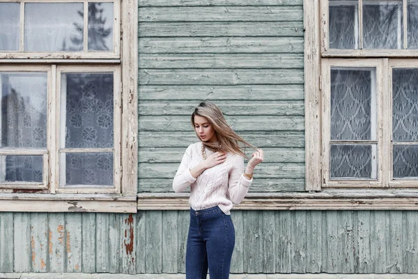 Mujer bonita en un suéter de punto en el fondo de la vieja casa de madera con ventanas —  Fotos de Stock