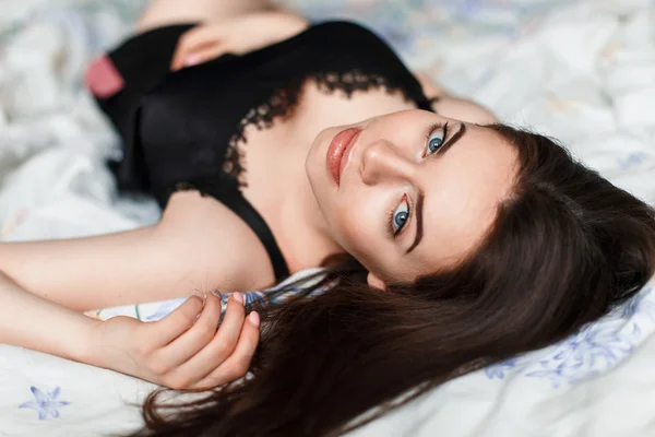 Hermosa chica sexy en lencería negra tumbada en la cama y mirando a la cámara — Foto de Stock